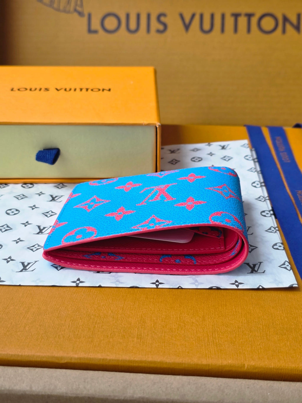 Small card wallet folded open, blue exterior with red fold and interior lining.