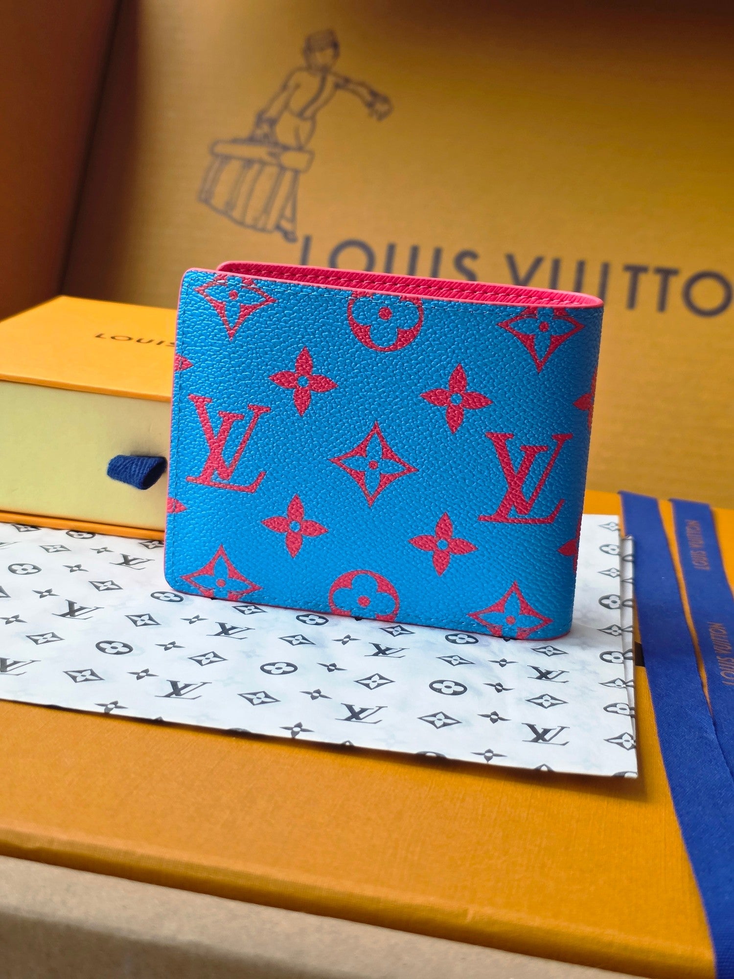 Small card wallet front view in blue monogram print with red piping and flap.