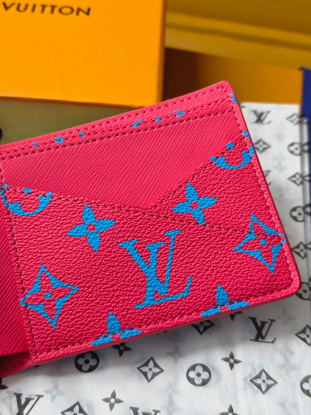 Small card wallet close-up showing blue monogram motifs on pinkish-red leather.