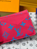 Small card wallet close-up showing blue monogram motifs on pinkish-red leather.