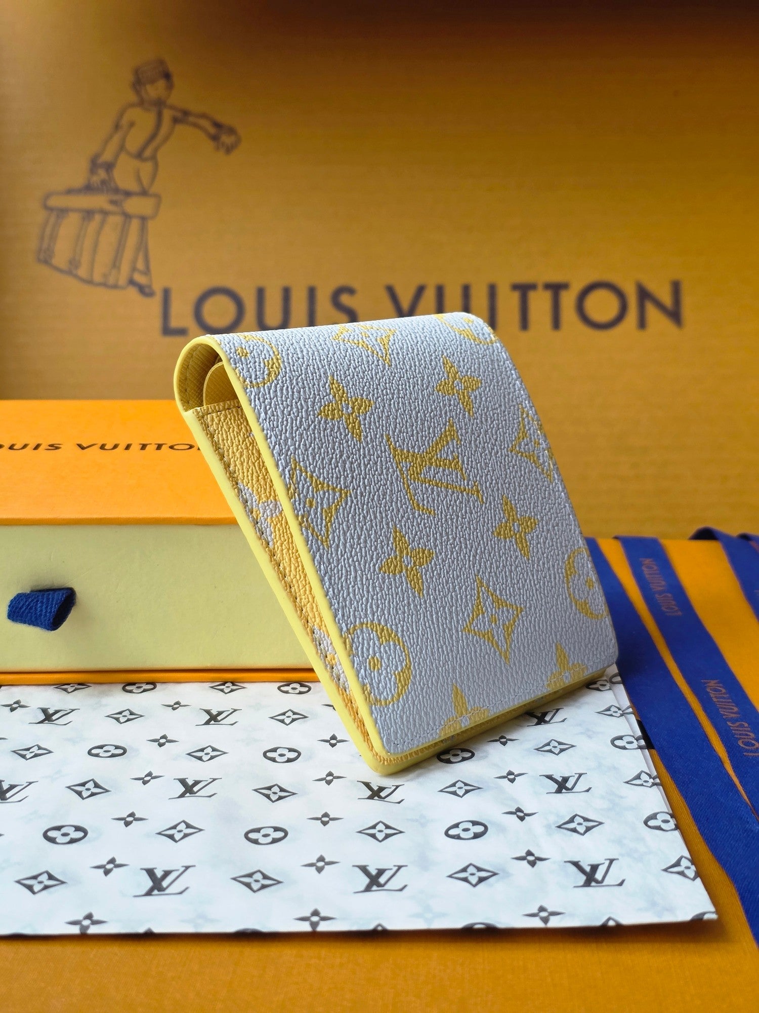 Small card wallet held at angle, blue with gold monogram and beige interior edge