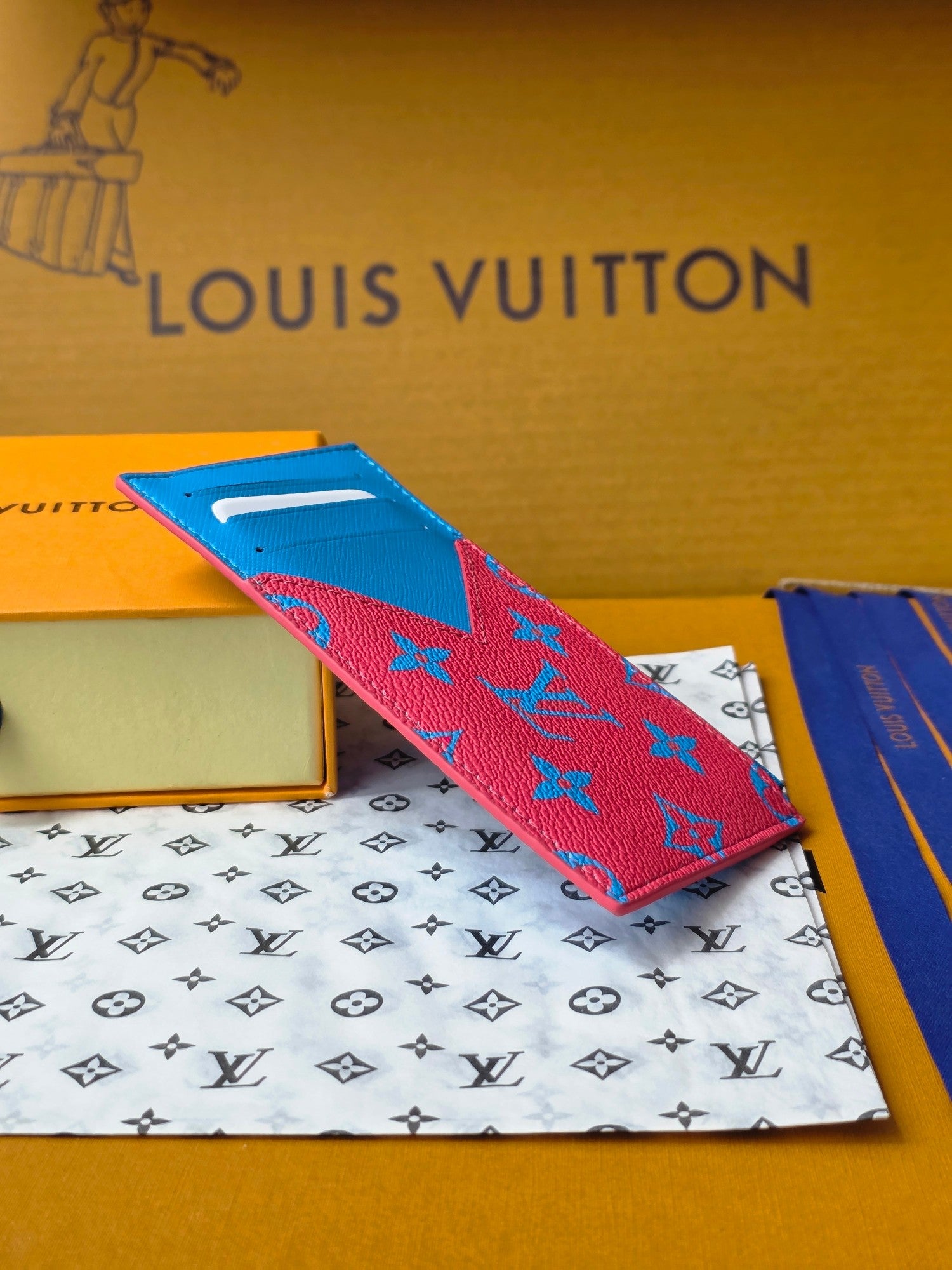 Small bag on angled view with blue top, pink monogram side panels, zip closure