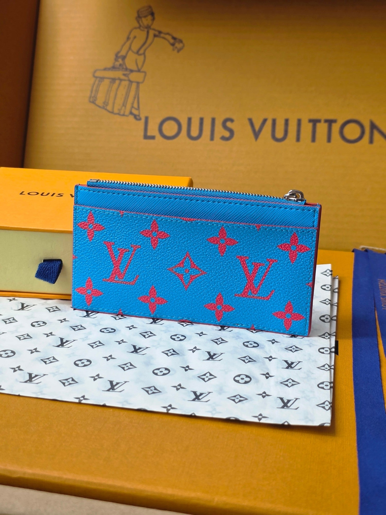 Small bag with blue front panel and multicolor monogram pattern, zip top closure