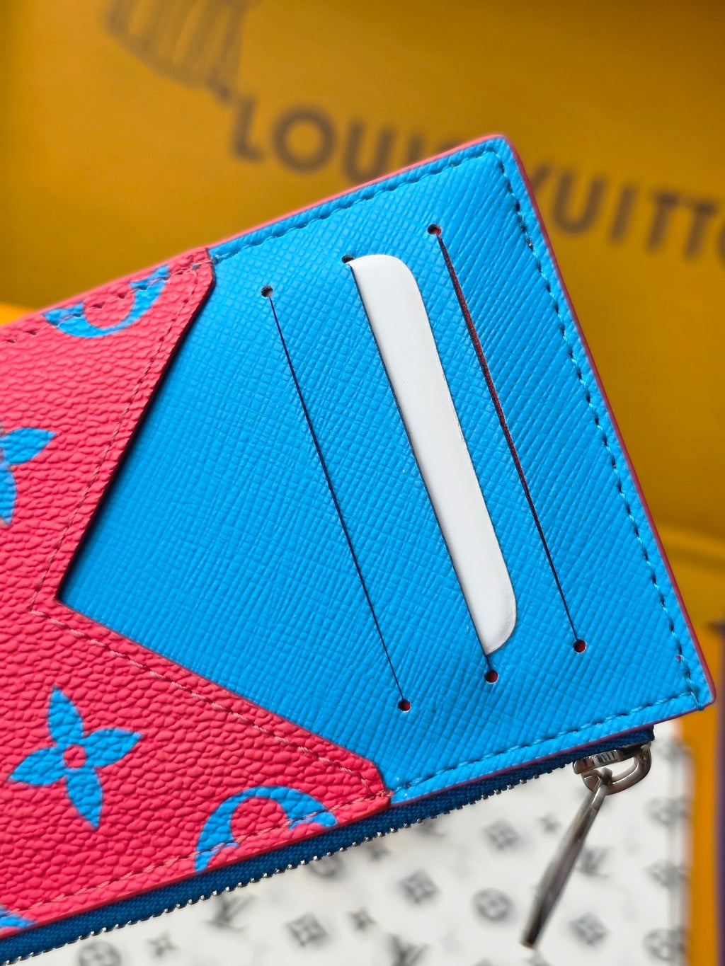 Small bag close-up showing blue leather tab and pink monogram panel with metal zipper