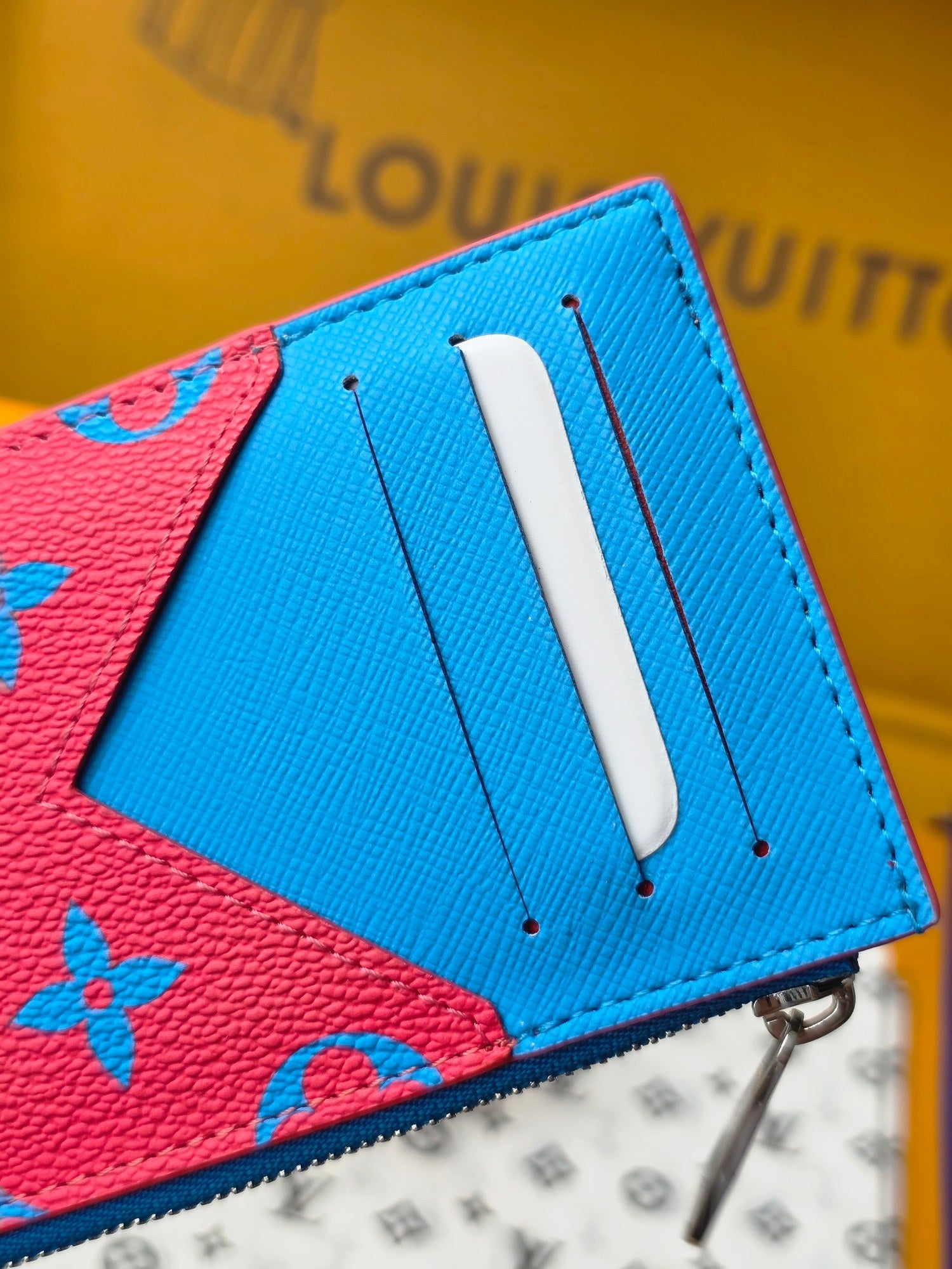 Small bag close-up showing blue leather tab and pink monogram panel with metal zipper