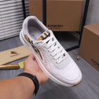White Burberry sneaker held in hand, showing plaid lining under the laces
