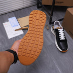 Luxury sneaker outsole view with textured orange-brown tread, black upper in frame