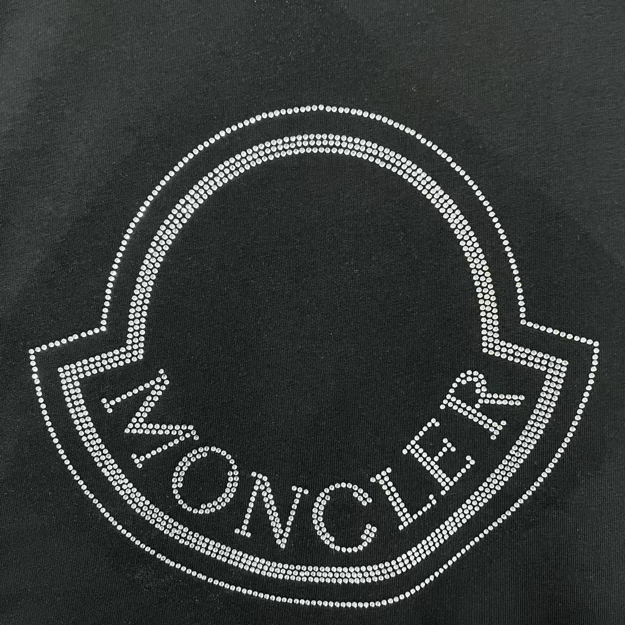 Close-up of rhinestone heart logo with Moncler text on a black sweatshirt