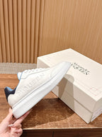 White low-top leather sneaker with blue heel trim and lace-up front.
