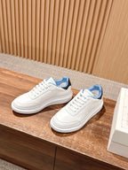 White leather low-top sneakers with blue collar and thick rubber sole.
