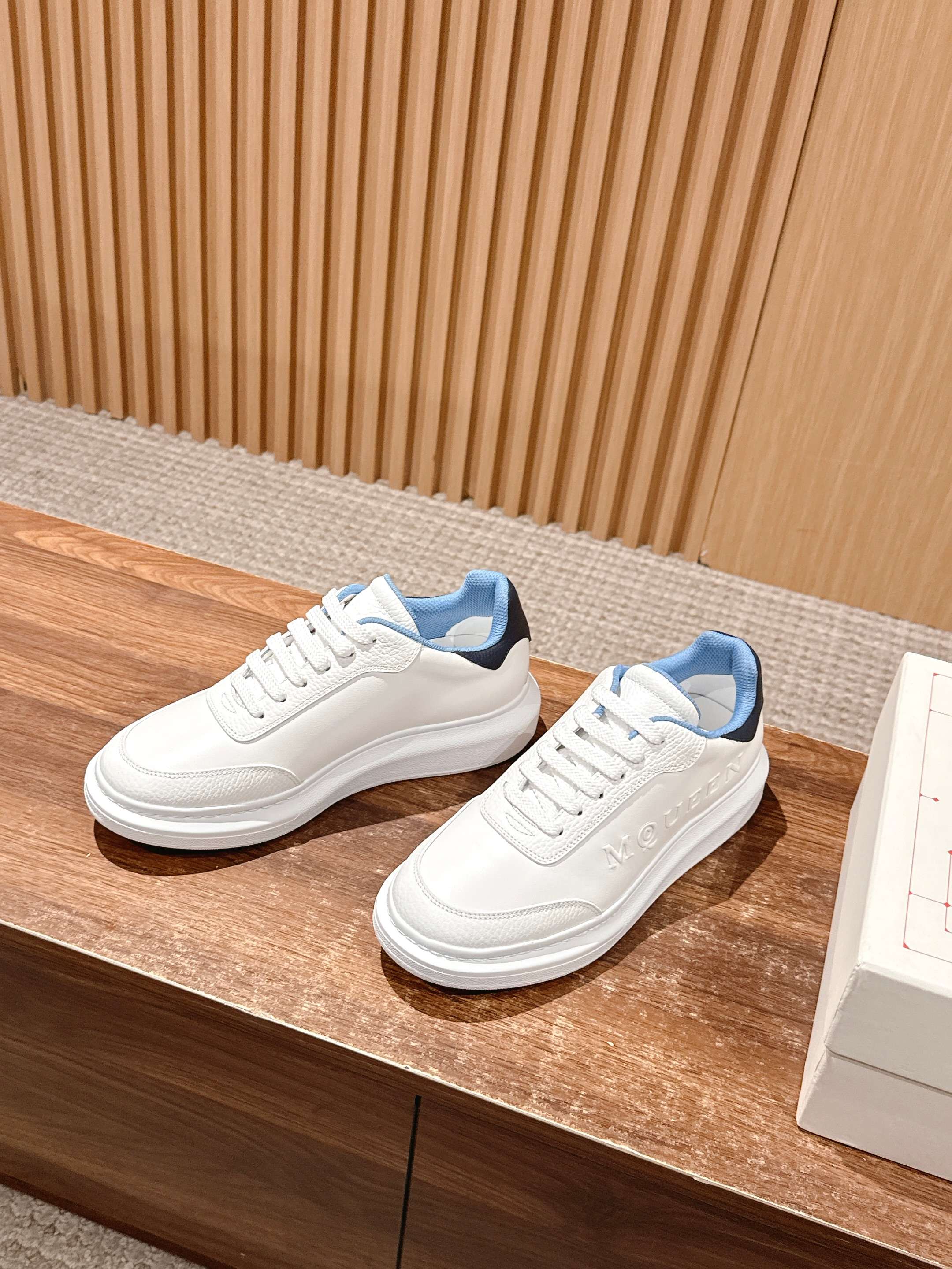 White leather low-top sneakers with blue collar and thick rubber sole.