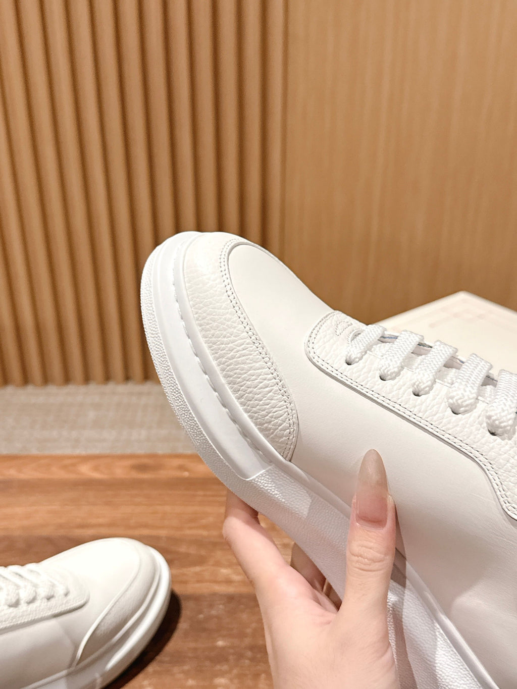White leather sneaker held by the heel, showing textured side panel and sole.