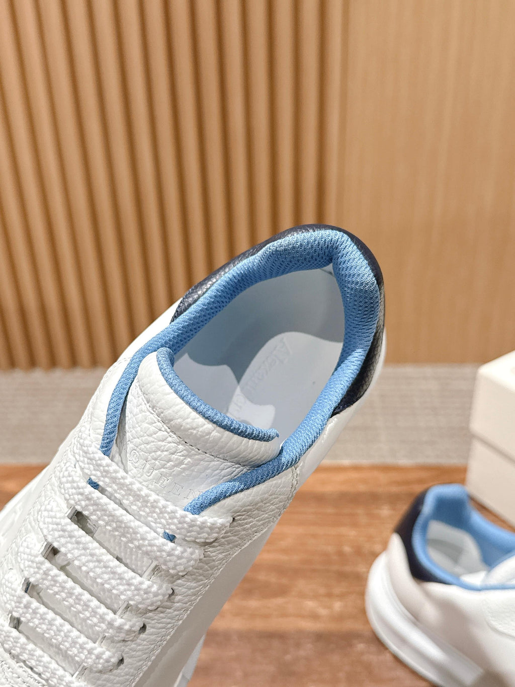 White sneaker with blue padded collar and lace-up front, close-up angle.