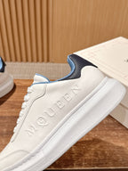 White leather sneaker with embossed Alexander McQueen logo and blue heel detail.