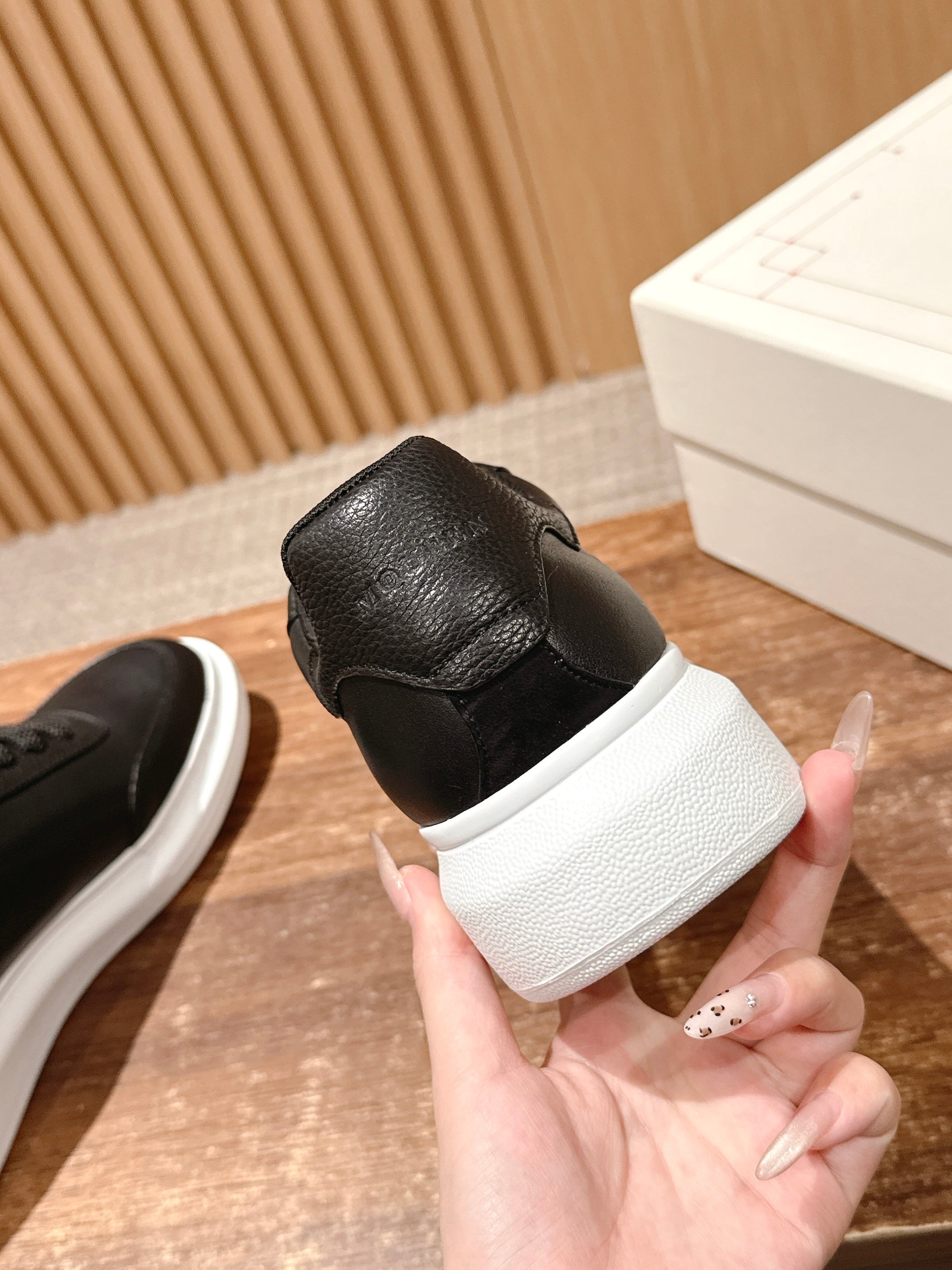 Black leather sneaker heel with white sole, held in a hand next to a box