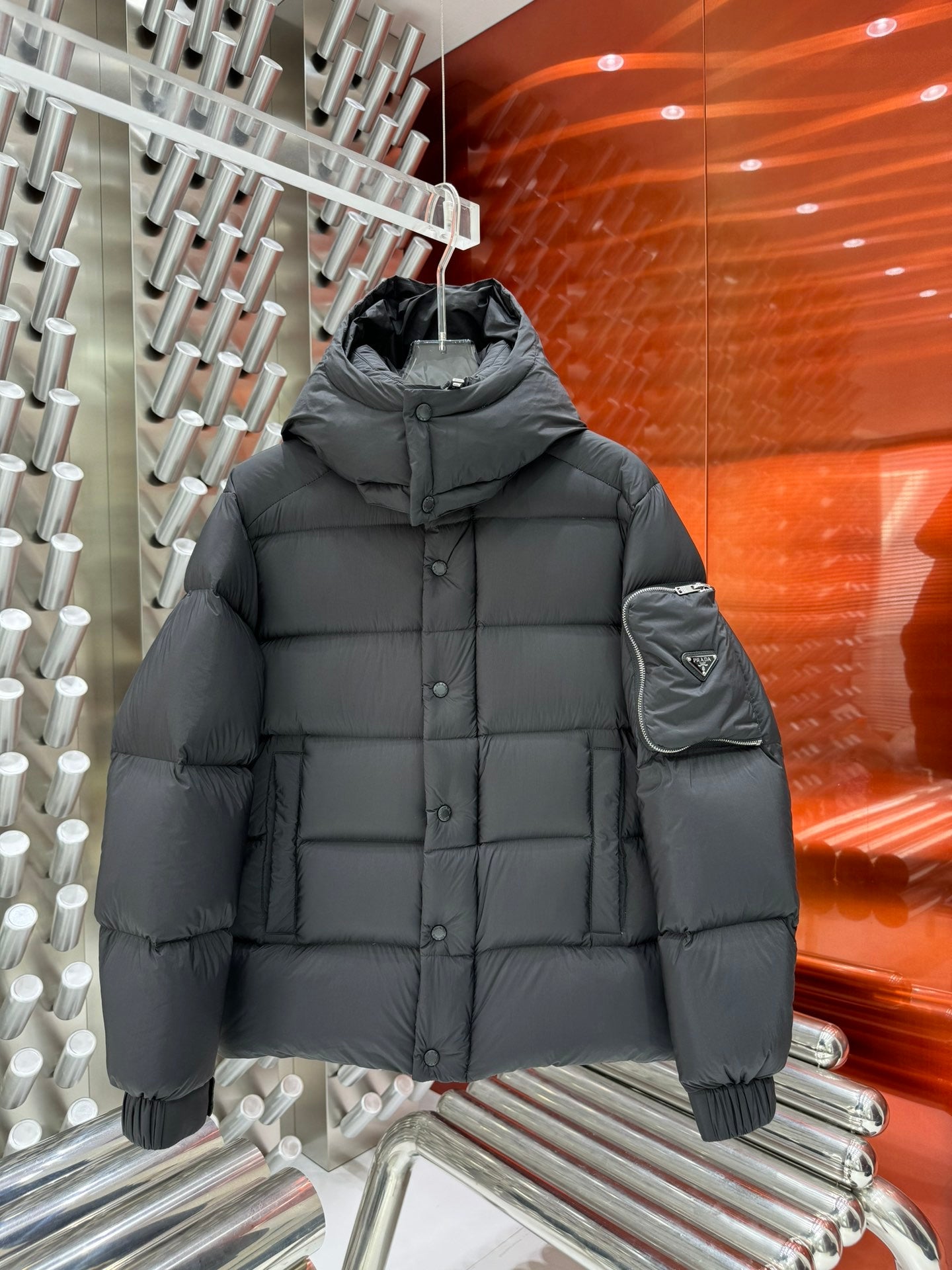 Long puffer jacket in dark gray with hood, button front, and sleeve pocket detail