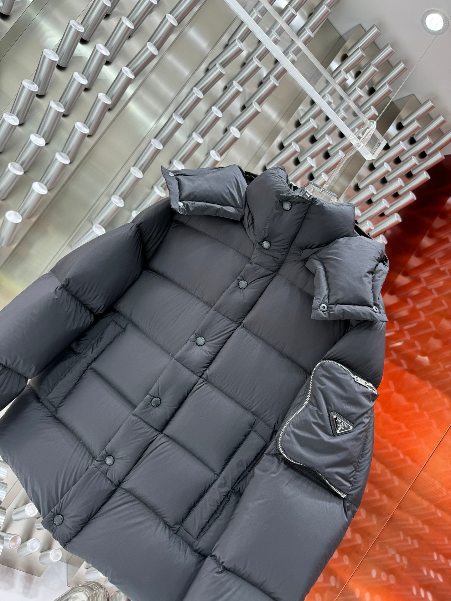 Long quilted puffer jacket in dark gray with hood and front buttons; sleeve pocket