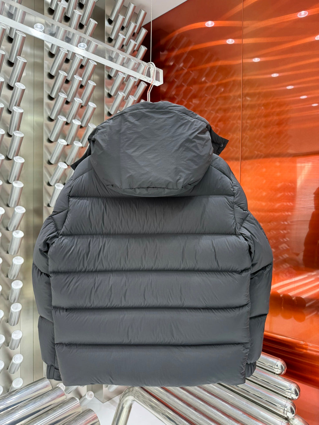 Back view of long puffer jacket in dark gray with padded hood and horizontal quilting