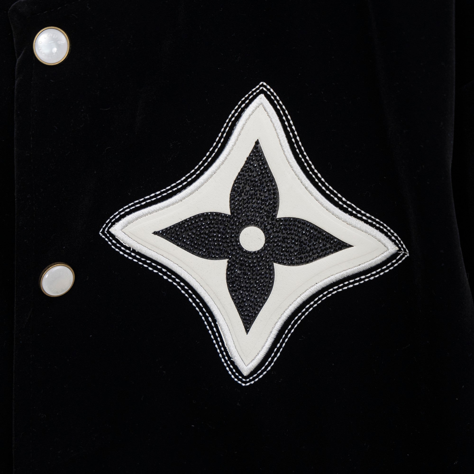 Black jacket with large white-and-black fleur-de-lis patch and snap buttons