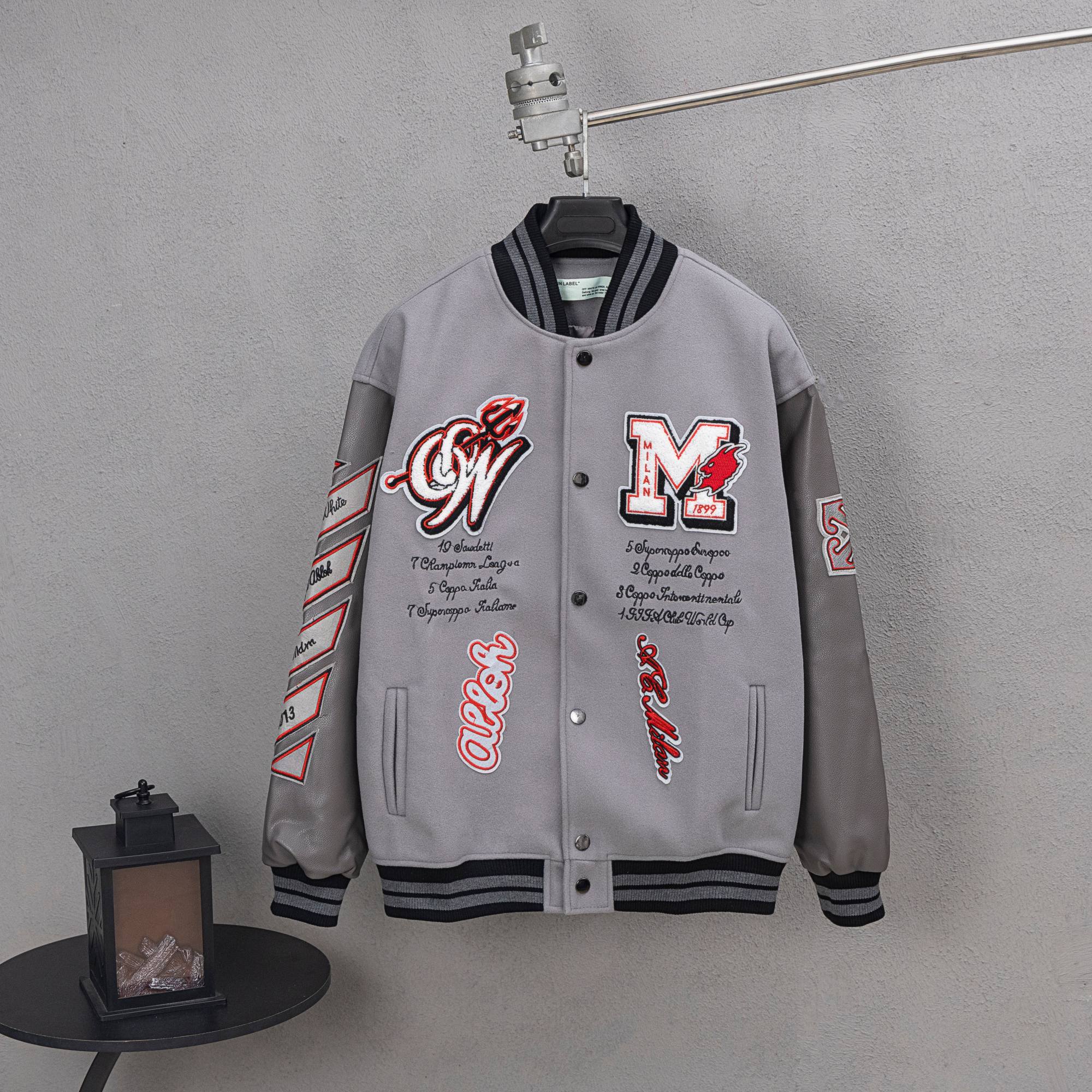 Off White varsity jacket, light gray with snap front, black striped cuffs, red graphic patches