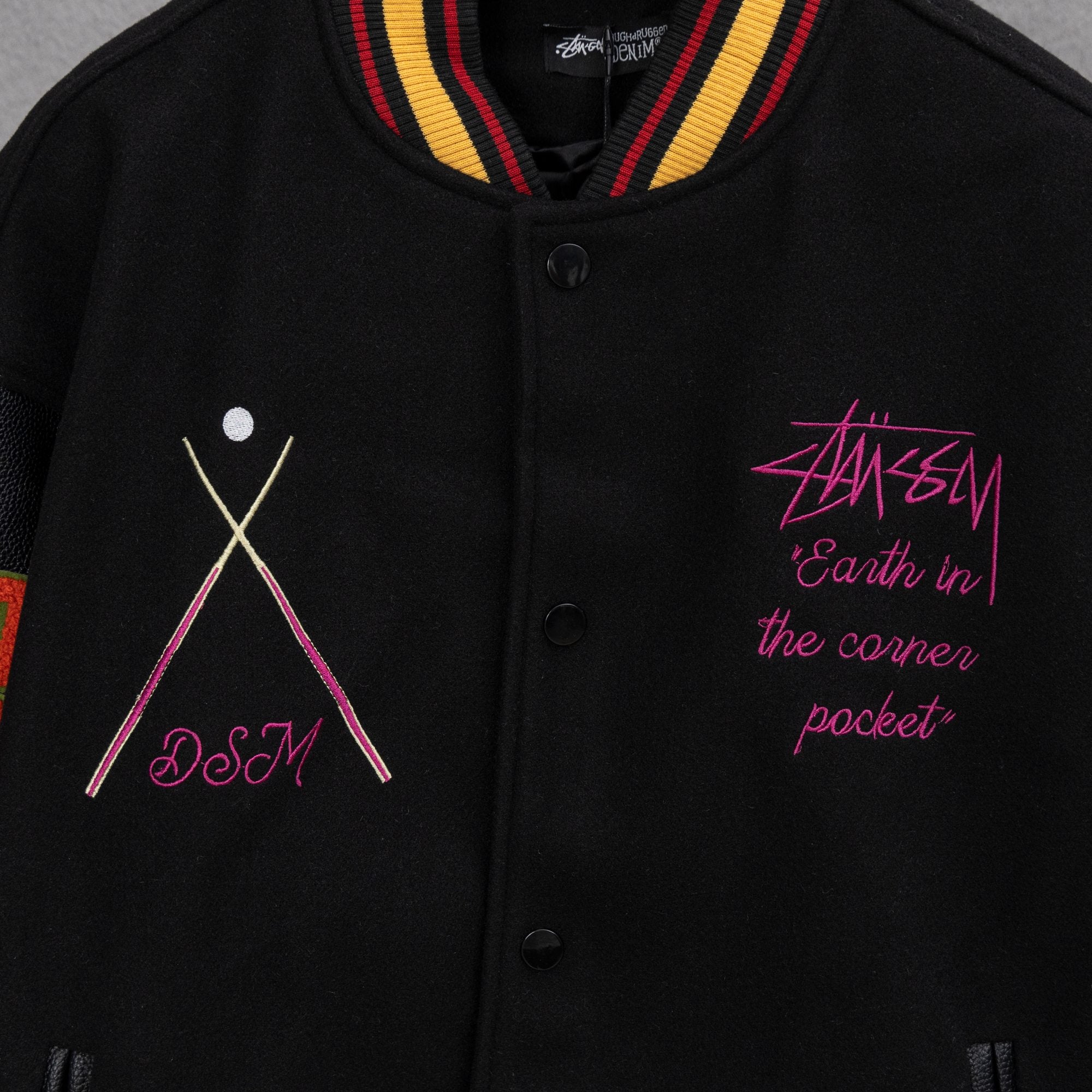 Black varsity jacket with striped collar, button placket, and pink graphic embroidery