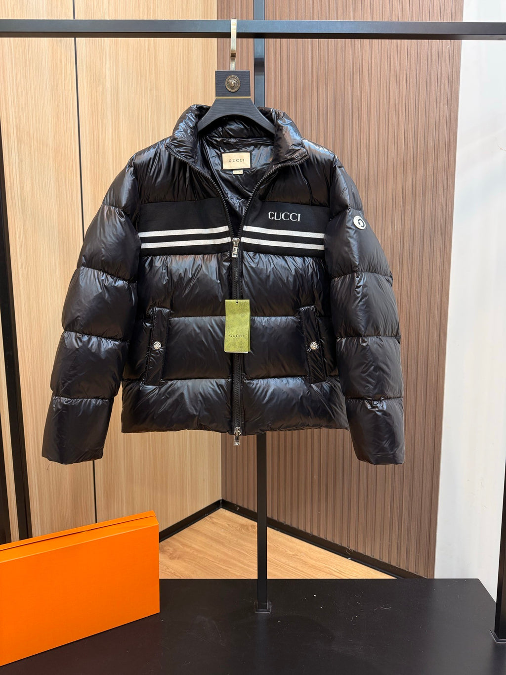 Black Gucci puffer jacket with striped chest band, zip front, hood, and side pockets.