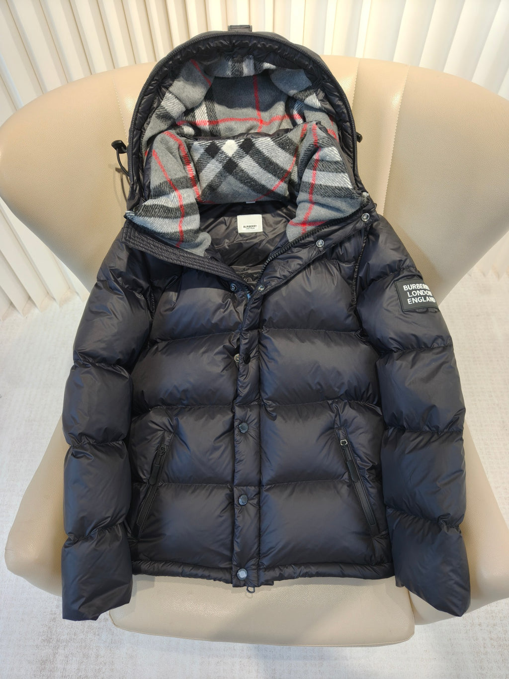 Puffer jacket close-up front, plaid hood lining, dark quilted body and zip closure