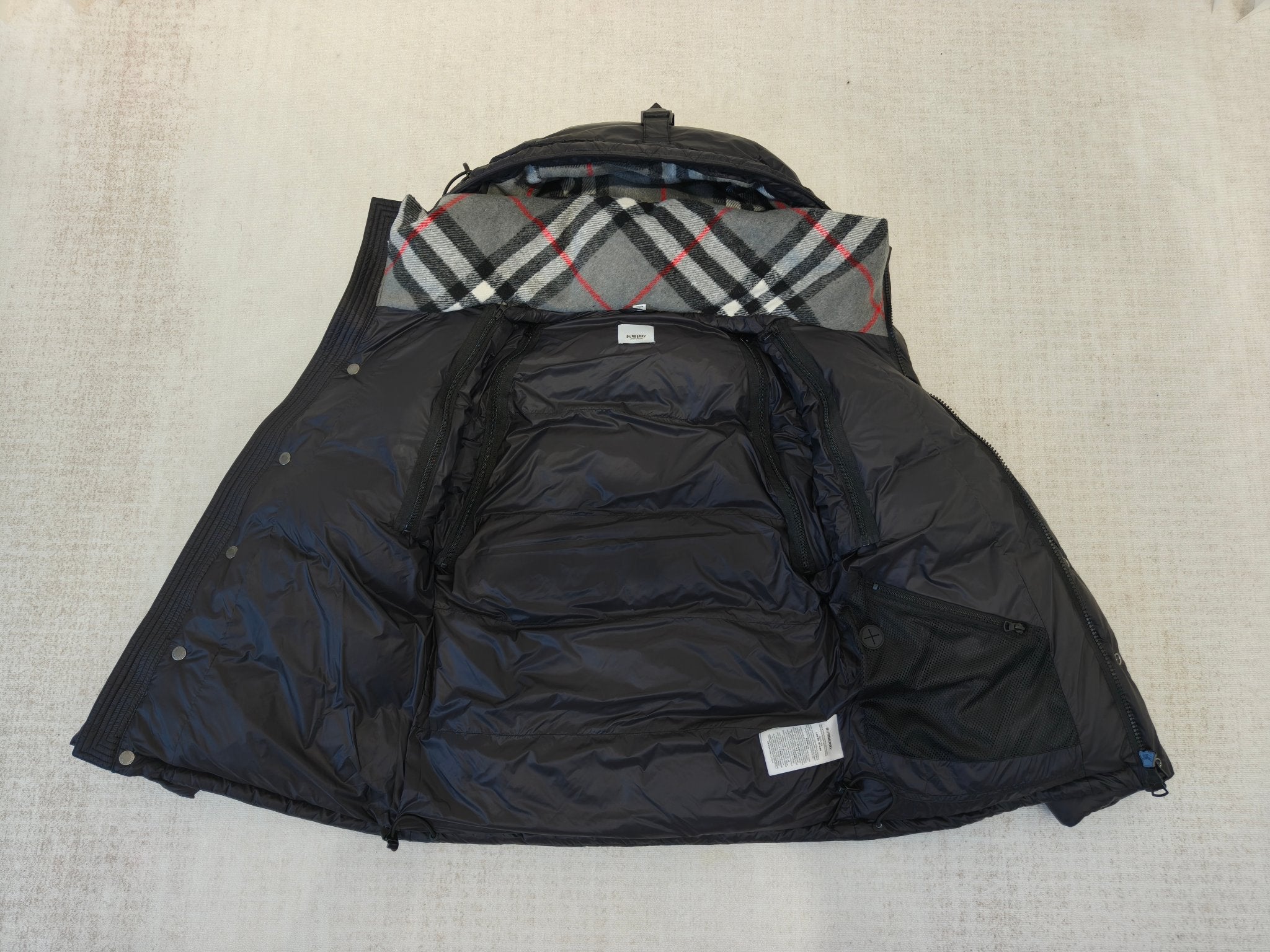 Puffer jacket interior view, dark lining with plaid hood yoke and two hanging tags