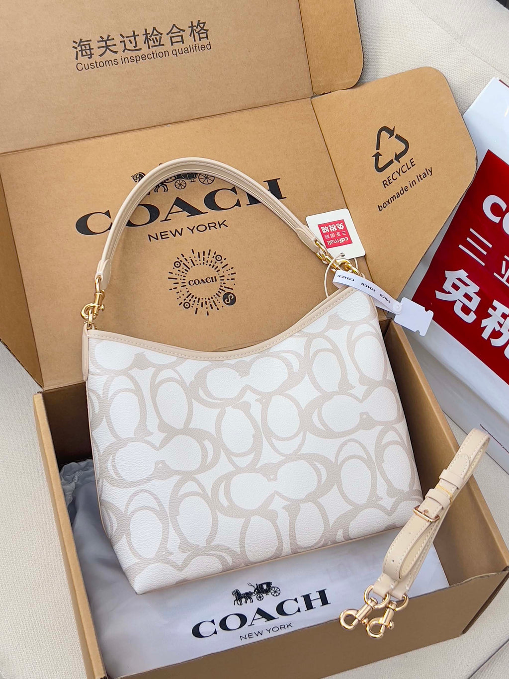 White patterned Coach hobo bag with top handle and shoulder strap, shown in gift box.