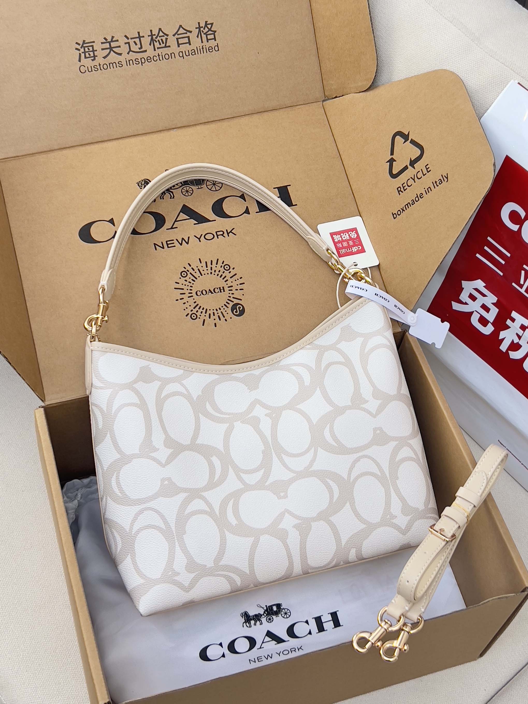 White patterned Coach hobo bag with top handle and shoulder strap, shown in gift box.