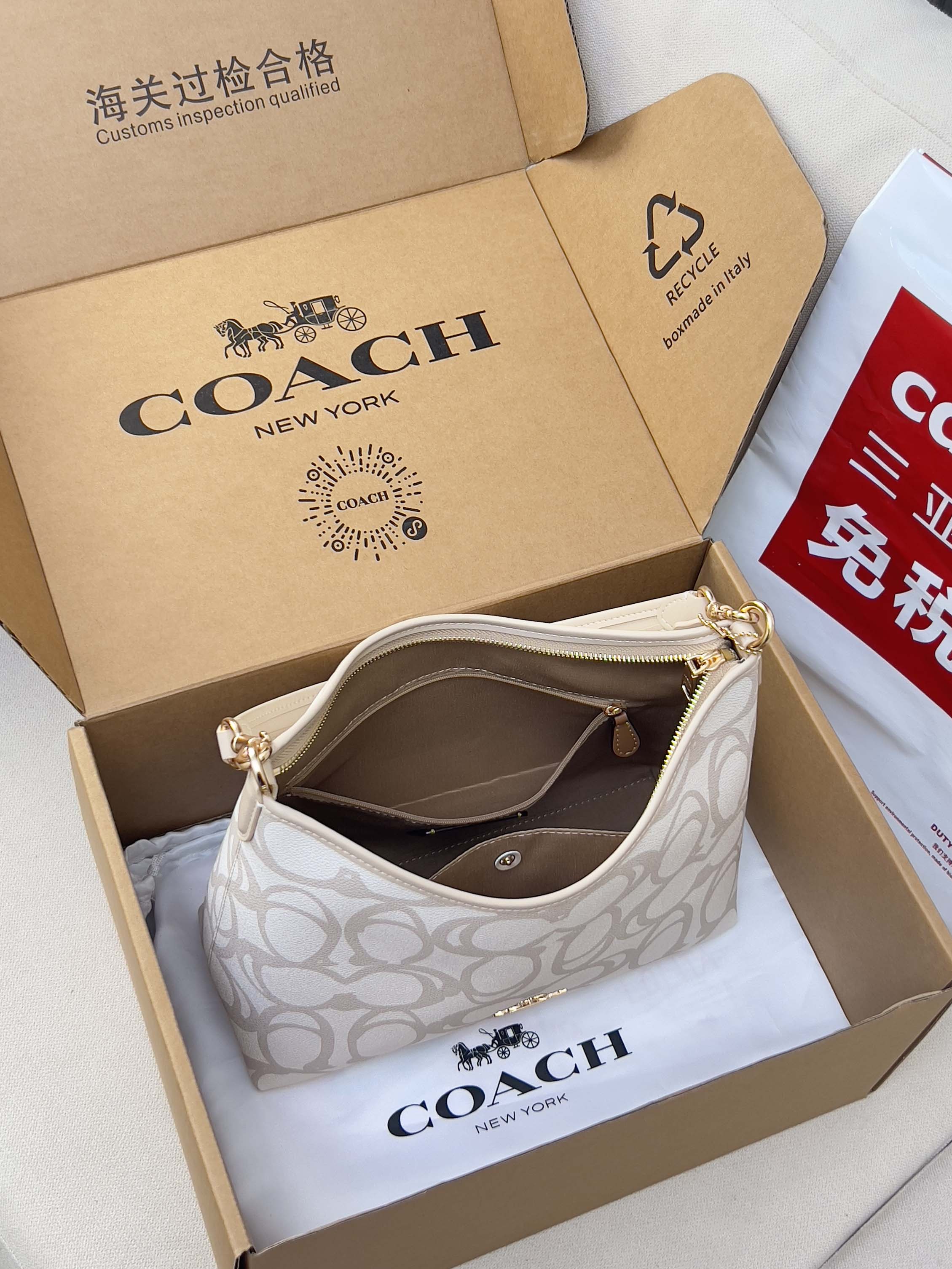 White patterned Coach hobo bag with top handle, open in gift box with strap.