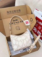 Coah crossbody bag with beige strap, white logo fabric, gold hardware, boxed display