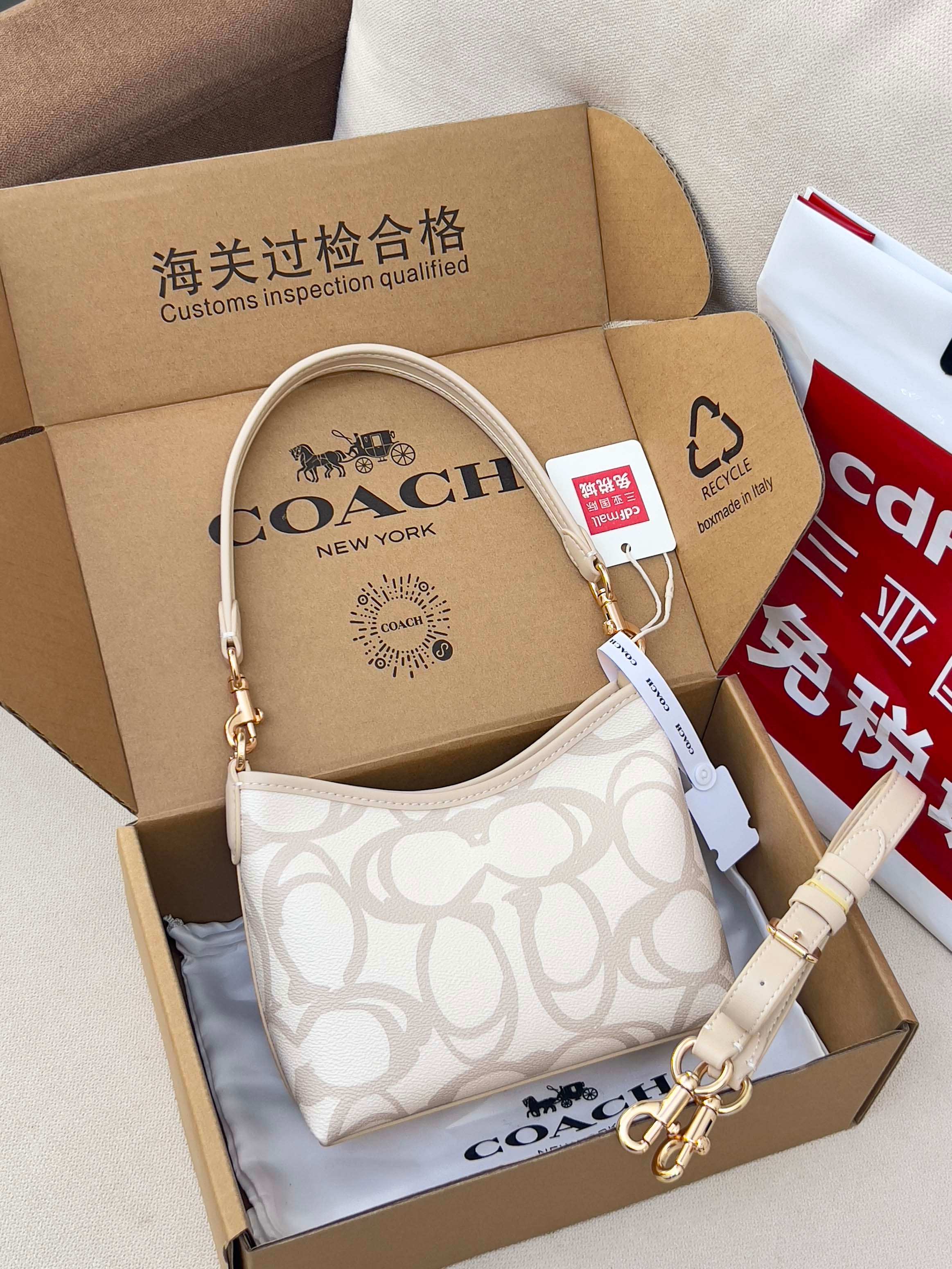 Coah crossbody bag with beige strap, white logo fabric, gold hardware, boxed display