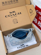 Light blue Coach mini shoulder bag in open box with patterned front and zipper