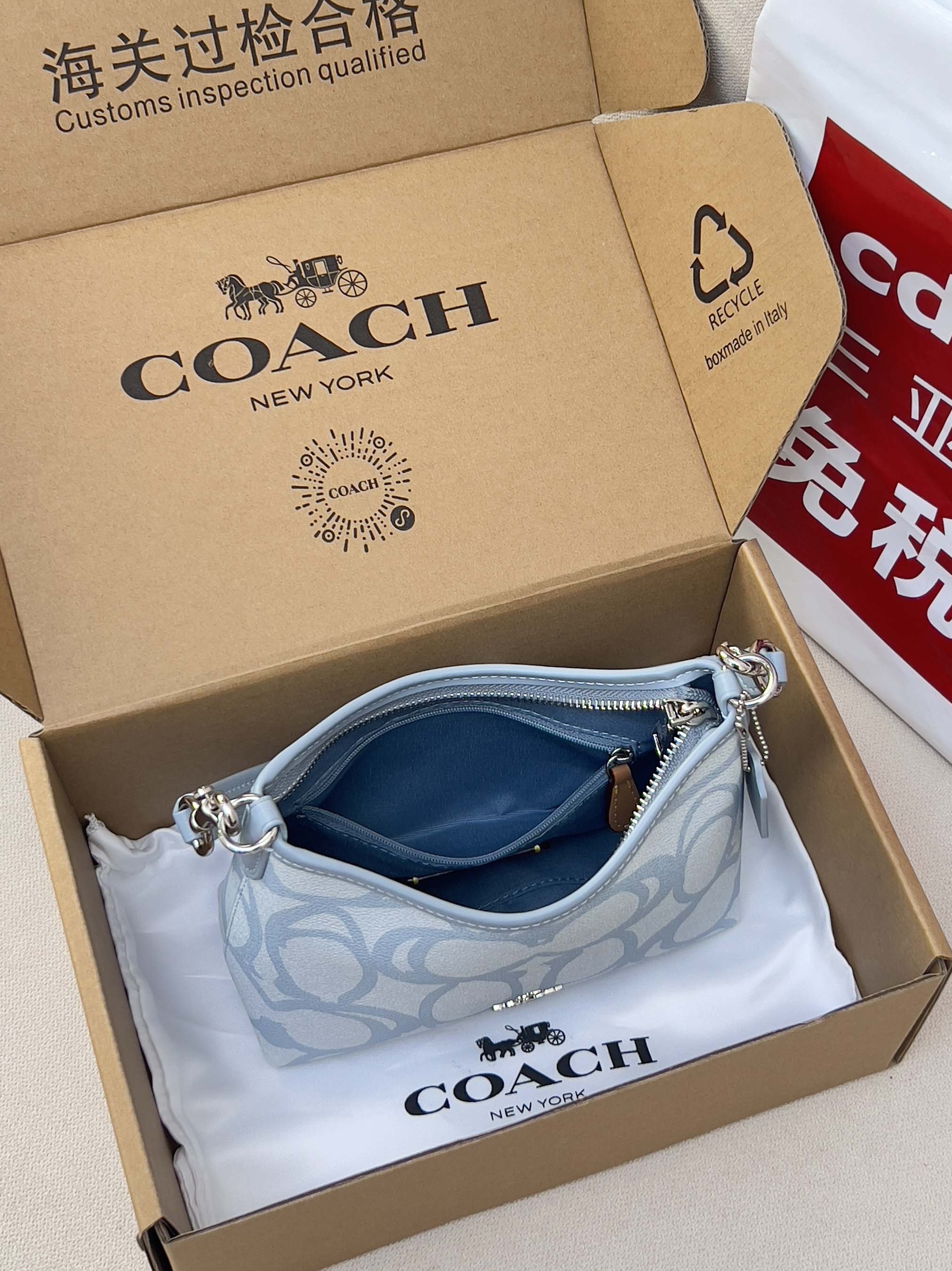 Light blue Coach mini shoulder bag in open box with patterned front and zipper
