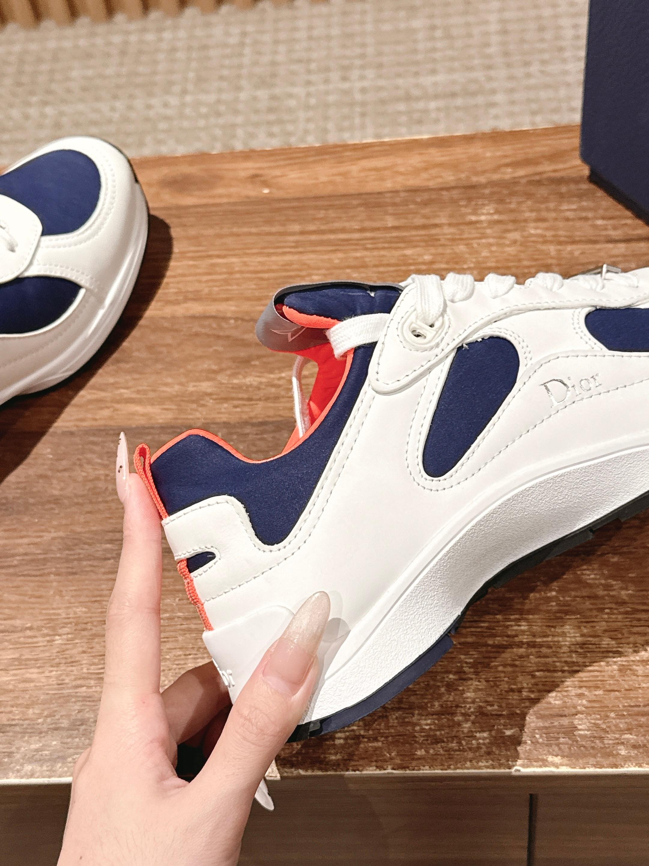 White and navy unisex sneaker with red-orange outsole and lace-up closure in hand