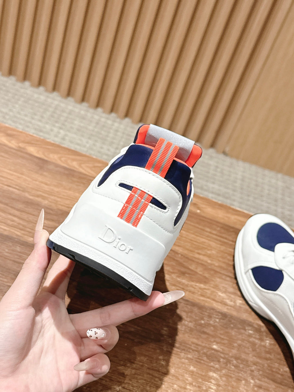 White unisex sneaker with navy upper, orange strap detail, and lace-up front