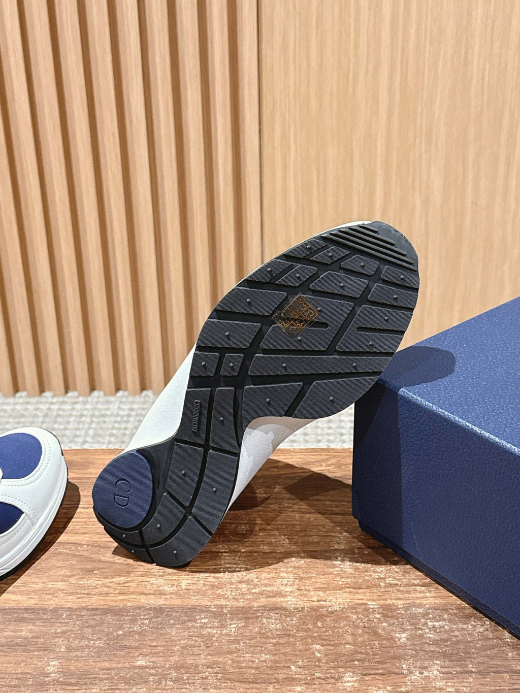 Textured rubber outsole of a white and navy unisex sneaker on a blue box