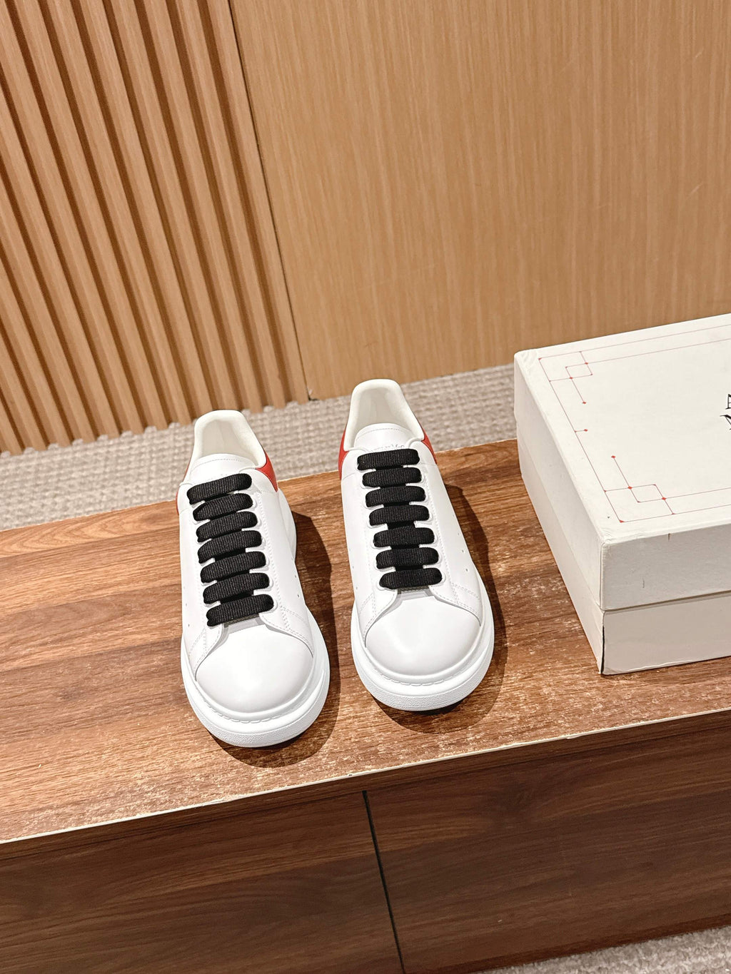 Pair of white sneakers with black laces and black lace tab details, red accent at heel