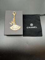 Chanel gold fan charm with chain and ring on gray gift box and black pouch