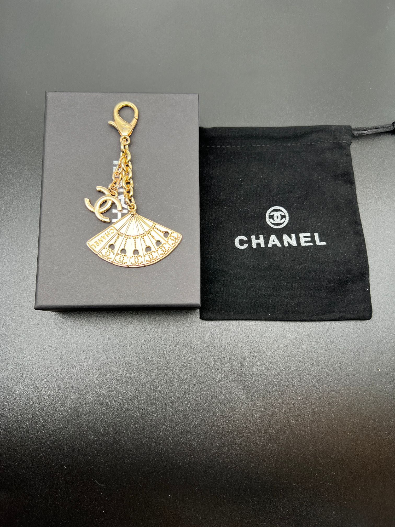 Chanel gold fan charm with chain and ring on gray gift box and black pouch