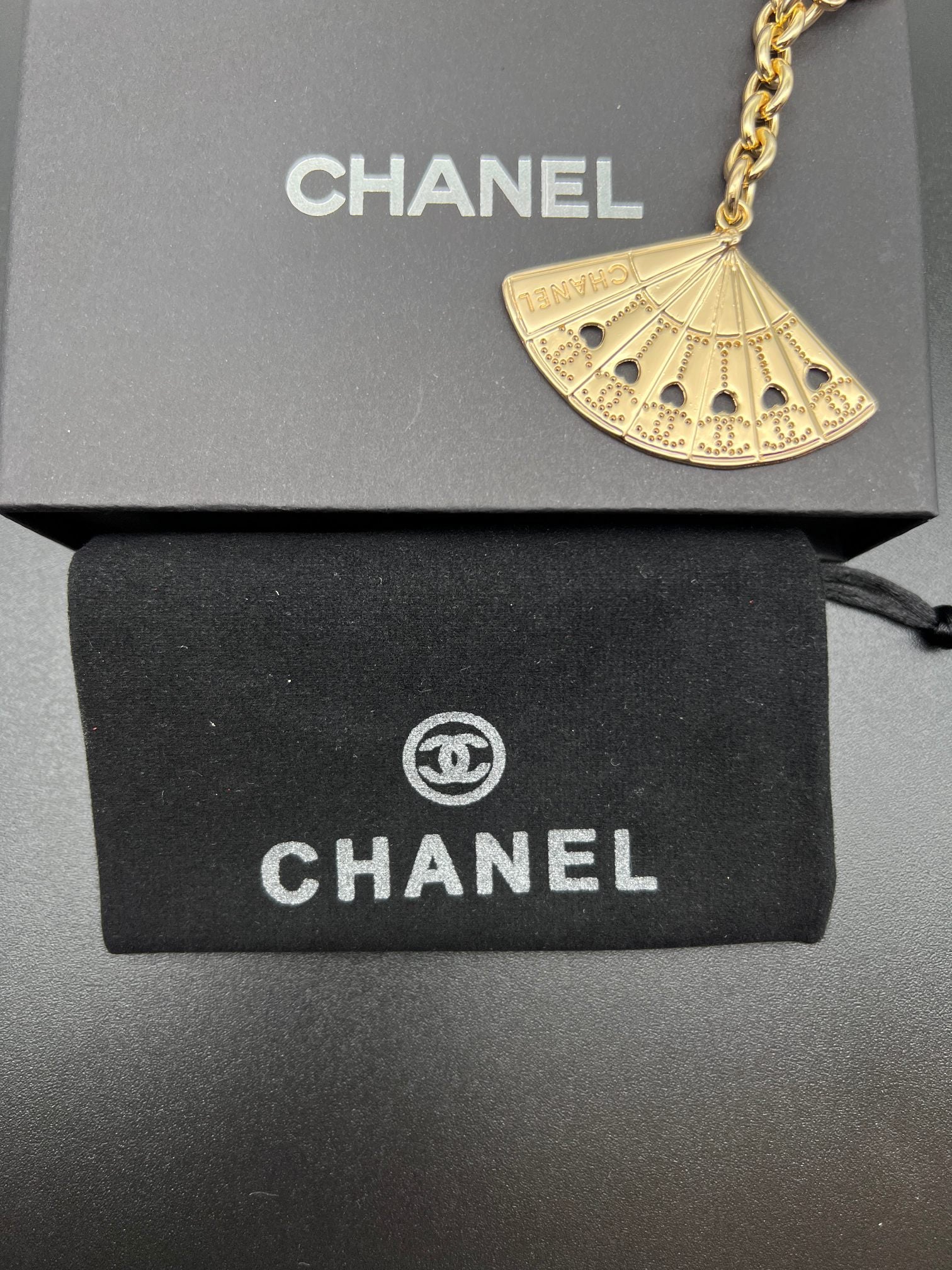 Chanel gold fan charm with chain and clasp over black gift box