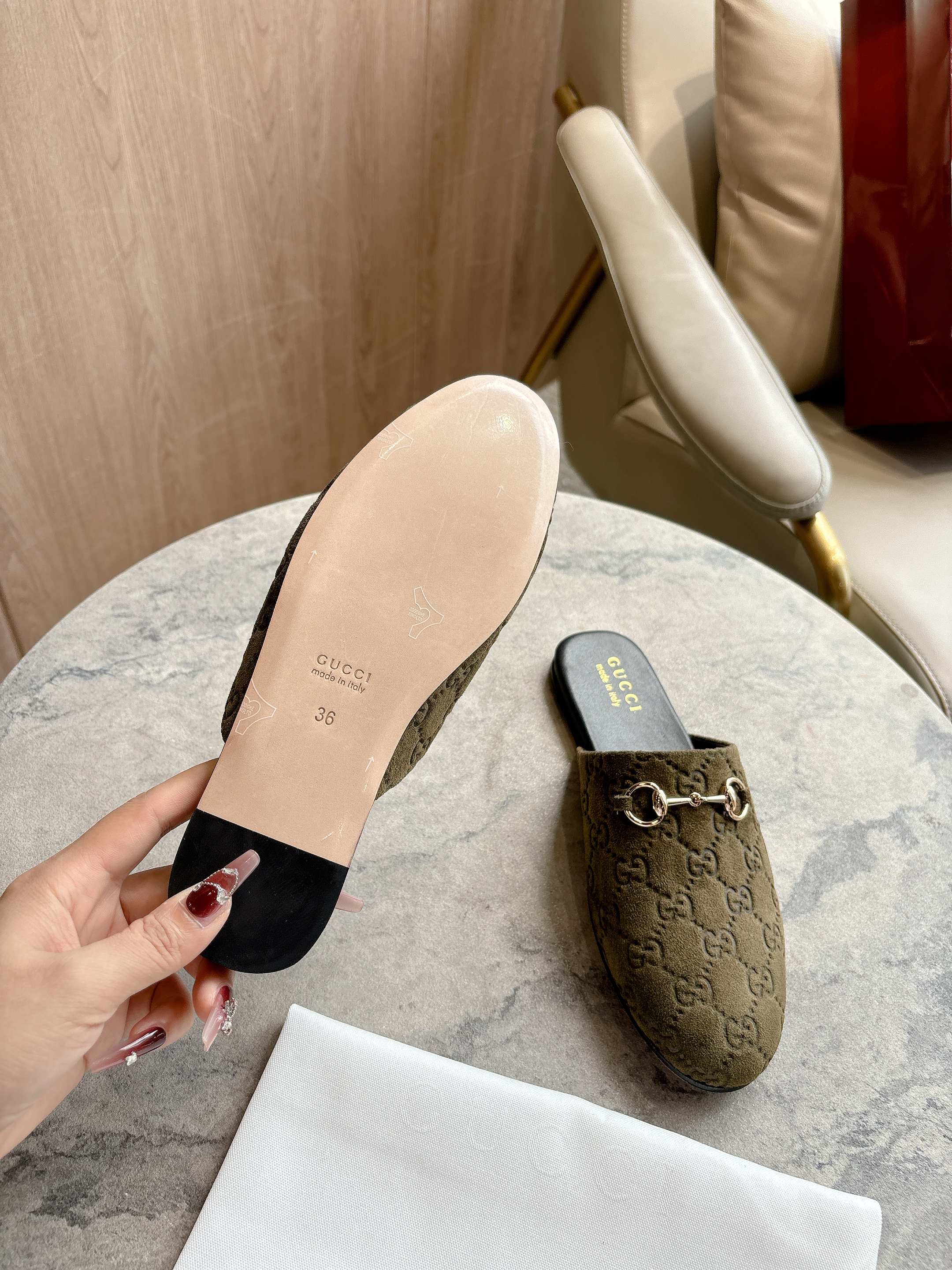 Gucci unisex slide mule with olive-brown GG upper and black insole; hand holds sole side.