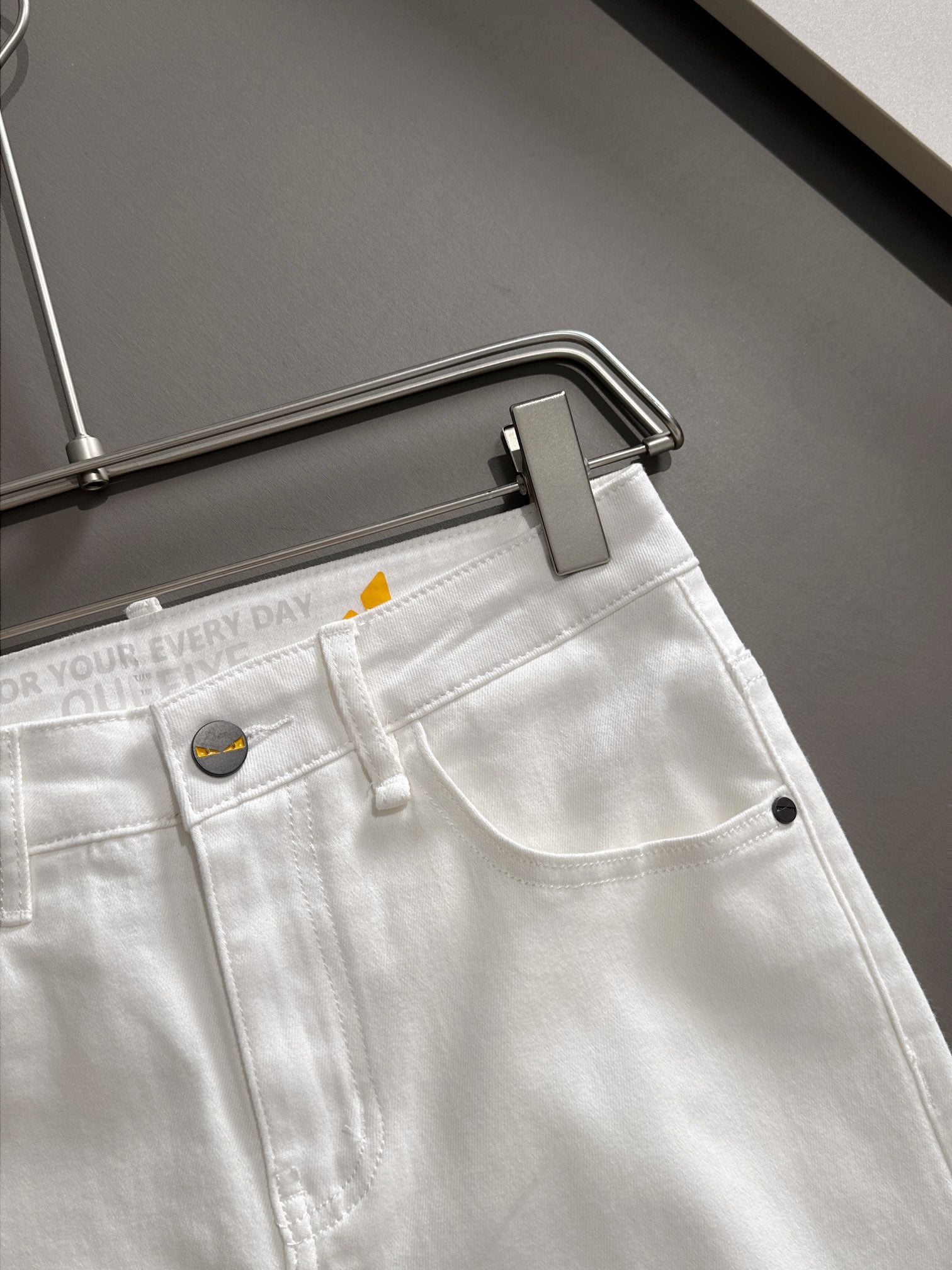 White denim pants close-up at waistband, button and belt loop detail