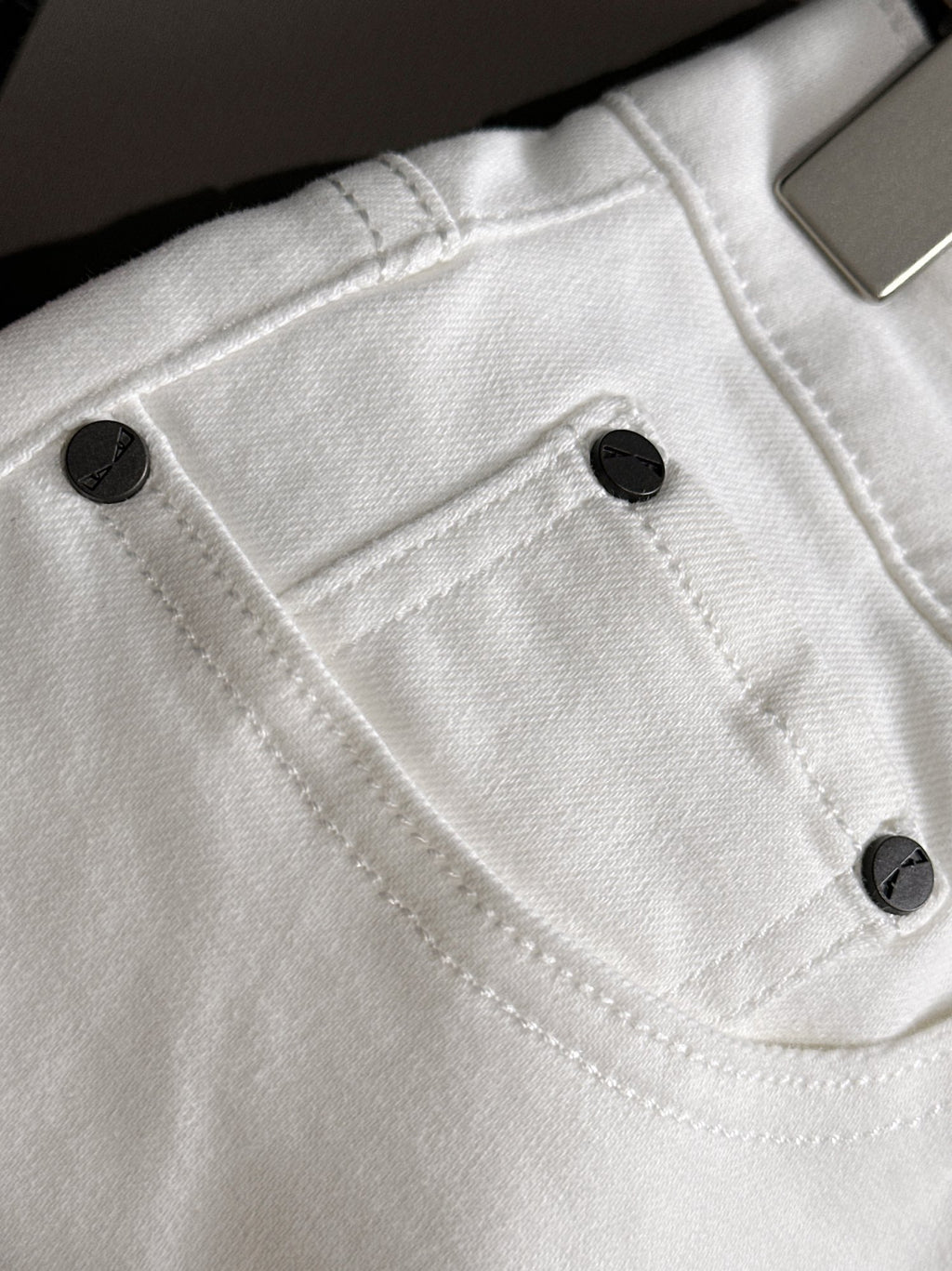 White denim pants close-up of front pocket and black button details