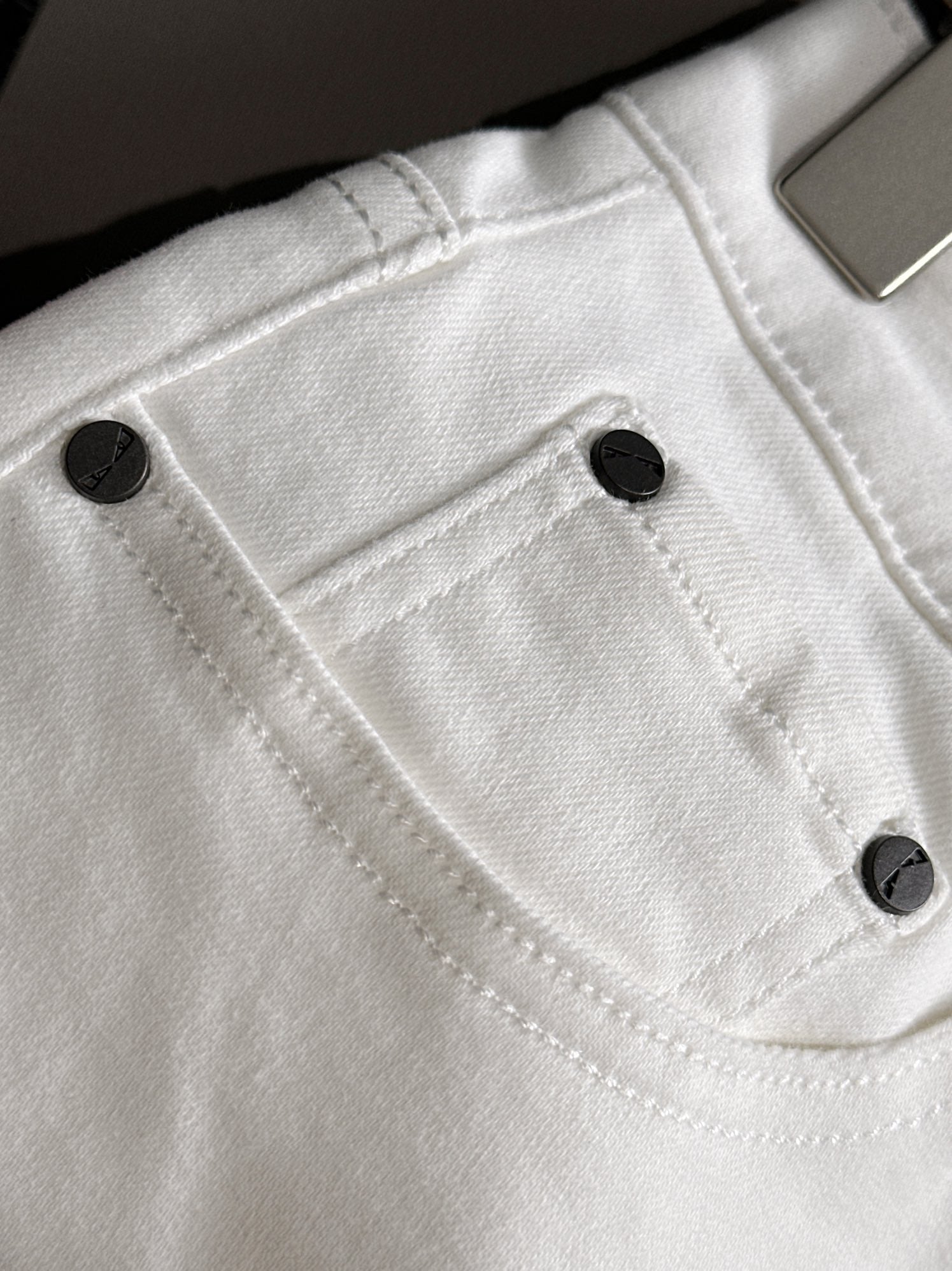 White denim pants close-up of front pocket and black button details