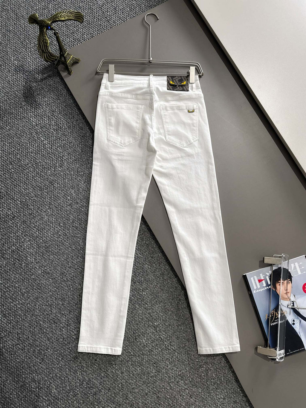 White denim pants hanging, front view with belt loops and button closure