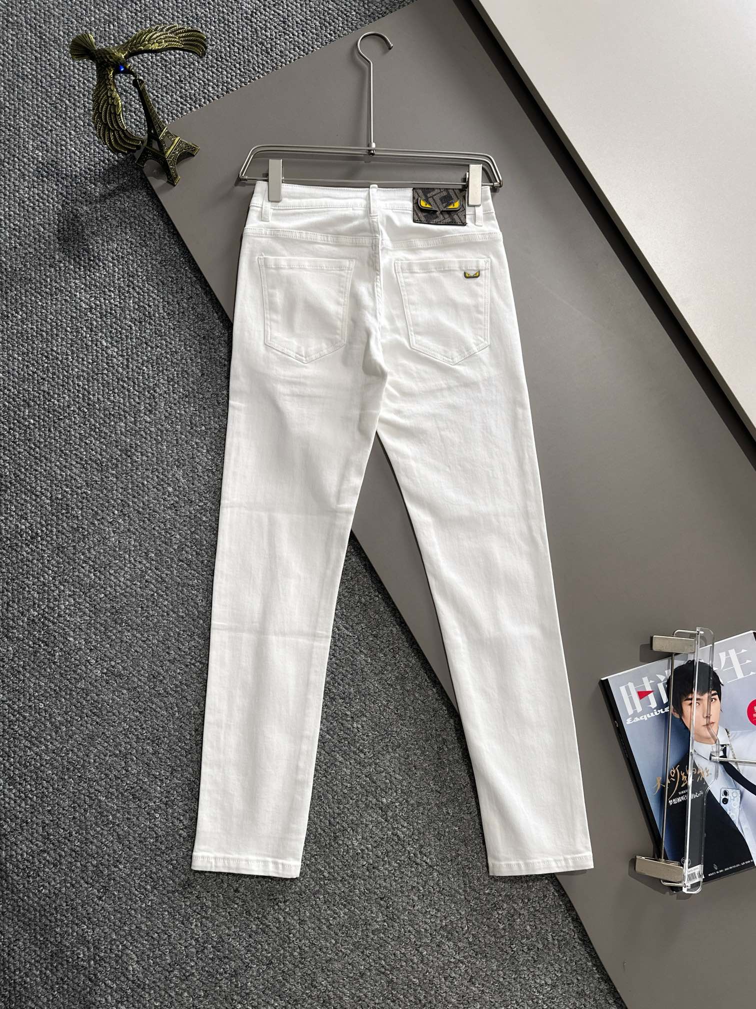 White denim pants hanging, front view with belt loops and button closure