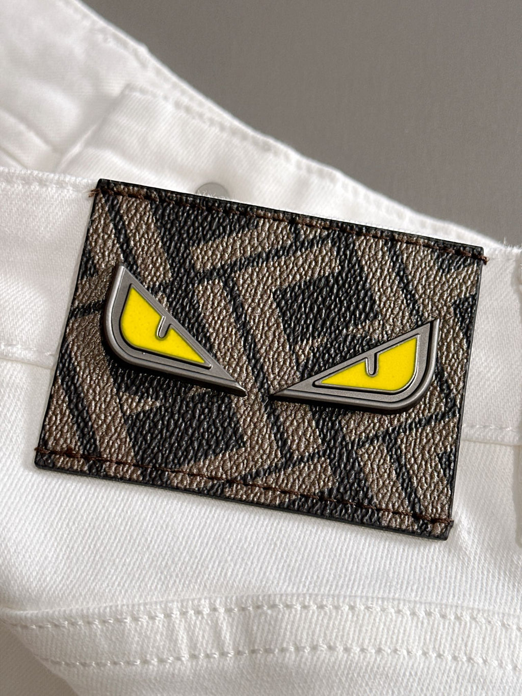 Rectangular logo patch on white denim pocket with yellow eyes and black border