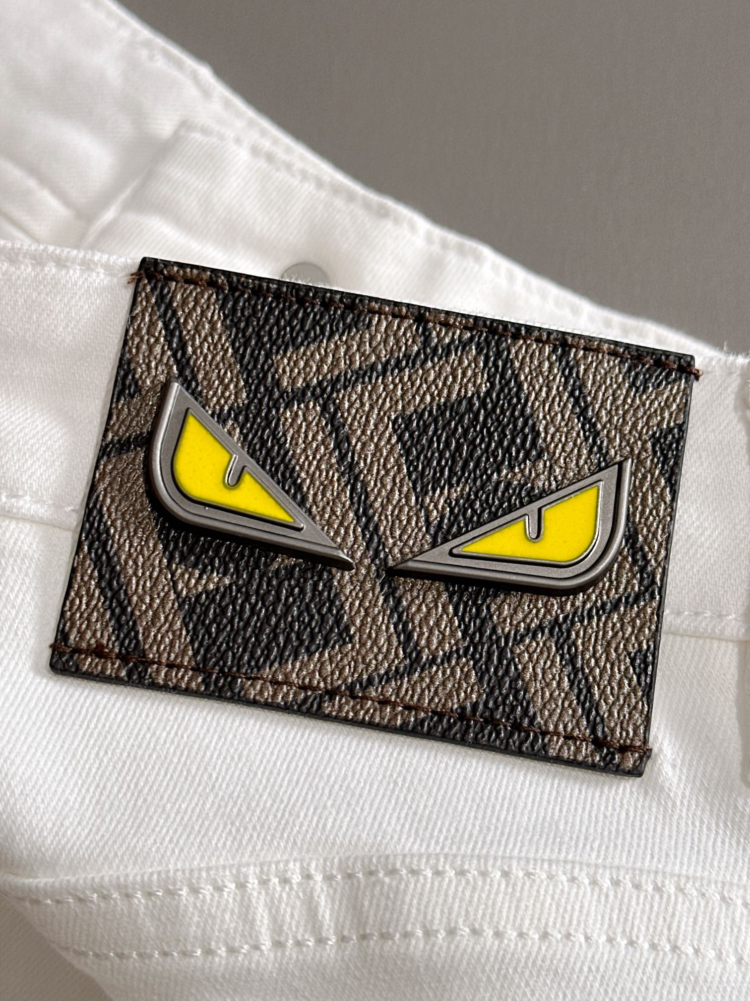 Rectangular logo patch on white denim pocket with yellow eyes and black border